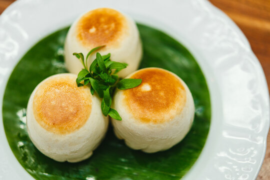 Three Pork and mushroom Chinese bao dumplings on a round green banana leaf on a white plate
