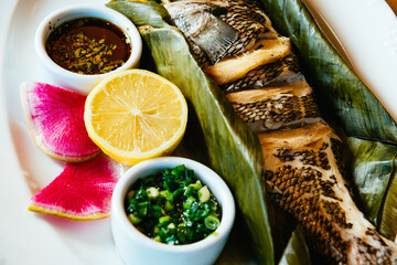 Whole Chinese style steamed fish in banana leaf with scallion relish, lemon, and spicy Vietnamese fish sauce, closeup