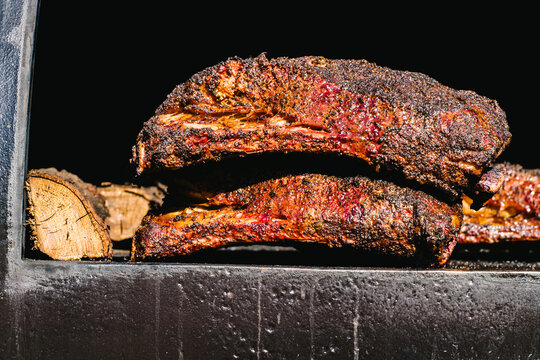 A blackened smoker holding two cooked briskets and a piece of firewood