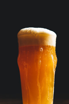 A hazy craft IPA beer with overflowing head in a tall glass against a black background, closeup