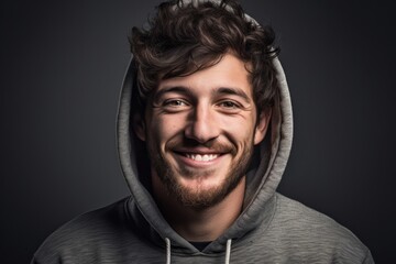 Headshot portrait photography of a grinning boy in his 30s wearing a comfortable hoodie against a minimalist or empty room background. With generative AI technology