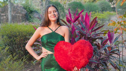 Young woman with red heart among red flowers on Valentine's Day
