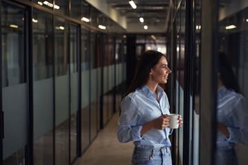 Cheerful corporate worker standing in office corridor during coffee break