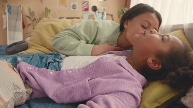 Handheld POV of African American preteen girl and her modern mother lying on kids bed together and having fun while recording video blog
