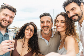 Smiling friends in their forties capturing joyful summer memories with a selfie on a docked boat. Group of diverse men and women enjoying a memorable moment together.
