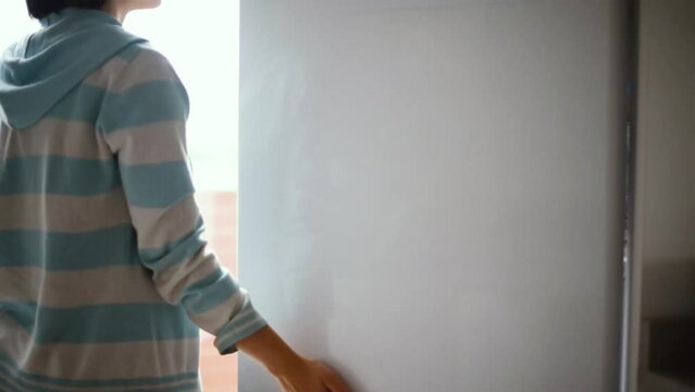 Una mujer camina hasta el refrigerador, se para pensando qu&eacute; tomar y finalmente agarra convencida un tupper con fideos. Gesto de movimiento de dedos mientras decide.