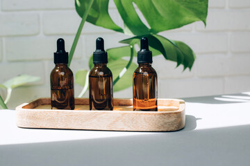 Amber bottles with facial treatment on a wooden tray with green leaves on backdrop. Front view