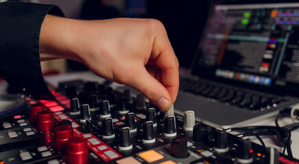DJ's hand over the laptop and mixing console controlling the sound settings.