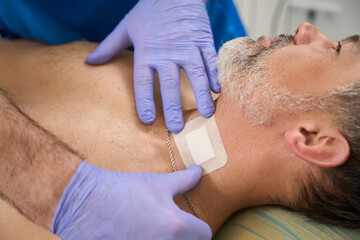 Obraz na płótnie Canvas Man doctor sticking patch to patient neck after injection