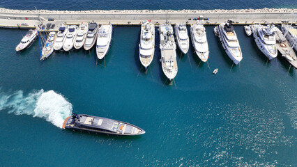 Aerial drone photo of small luxury yacht manoeuvring to dock in Mediterranean port with anchored...
