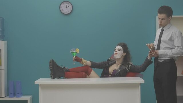 A woman sits in an office chair with her legs up on the desk. Cosmetic mask on woman's face, cocktail in hand. An office worker stands nearby and does a manicure. HDR BT2020 HLG Material