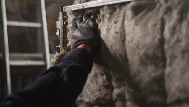 Worker in gloves adjusts glass mineral insulation on detail with metal frame at construction site closeup. Employee puts warmth protection on equipment in boiler room