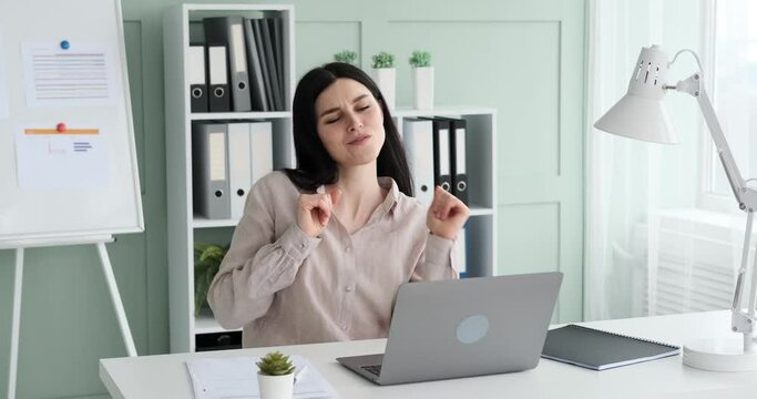 Businesswoman in a shirt sitting at her desk in the office, celebrating a successful deal or the end of a workday by dancing in her seat. Her joyful and satisfied expression highlights the happiness.