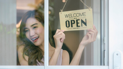 Woman store owner turning open sign broad through the door glass and ready to service. Small...