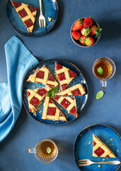 Crostata is a traditional Italian open fruit tart with strawberry jam on blue plates, tea in glasses, fresh strawberries, napkin over blue surface. Flat Lay, top view