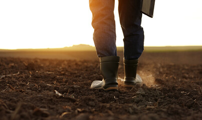 Agriculture. Cropped shot of back view businessman farmer in rubber boots walks along plowed field...