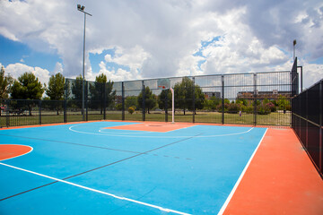 Empty outdoor basketball court in the garden and blue sky. Blue red basketball court for soccer, outside in sunny summer day. A modern playground for sports without people. Playground flooring. - Powered by Adobe