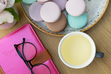Cup of green tea with pastel colors pastry macarons on a wooden table top view. Business in cafeteria concept.