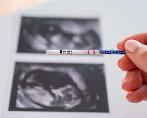 Woman holding a positive pregnancy test on the background of a photo with an ultrasound. 
