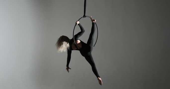 A skilled Caucasian performer on the aerial hoop. With long hair flowing and a confident demeanor, she executes intricate acrobatic maneuvers with grace and precision.