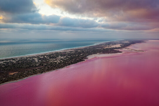 Pink Lake in Port Gregory in Western Australia, colored water by bacteria and algae, beautiful contrast between the blue ocean and pink water, clouds on the sky, aerial view