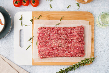 Board with fresh minced meat and rosemary on grey grunge background