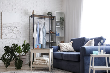 Interior of light room with sofa, shelving unit and clothes