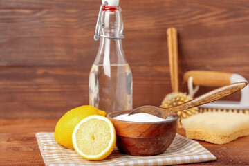 Bowl of baking soda, lemons, vinegar and cleaning supplies on wooden background