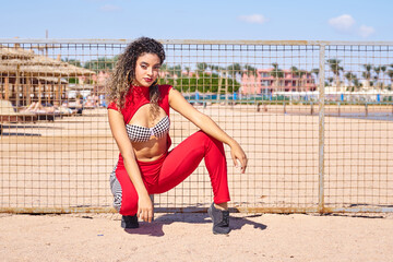 Sexy woman with slim figure in red suit and curly hair.Attractive Formula 1 beautiful model  Hostess posing on the beach.Bikini model.