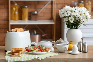 Modern toaster with crispy bread slices, delicious sandwiches and cup of tea on table in kitchen