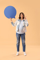 Young pregnant woman with blank speech bubble pointing at something on beige background