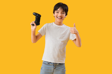 Little boy with game pad showing thumb-up on yellow background