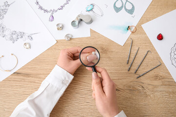 Female jeweler examining ring on wooden table, top view