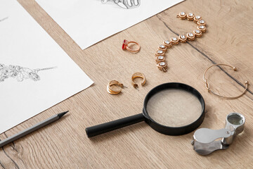 Jeweler's magnifiers with accessories and drawings on wooden table, closeup