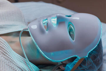 LED light anti-aging mask for facial skin care in a spa slow motion. A woman lies on a couch in a...