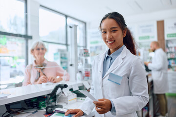 Obraz premium Happy Chinese female pharmacist working in pharmacy and looking at camera.