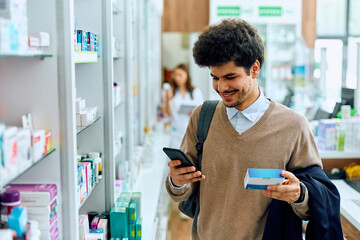 Happy Muslim man using mobile phone while looking for medicine in pharmacy.
