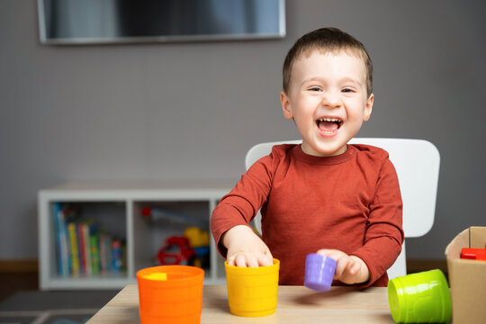 A cute happy little toddler boy of two years old sits at a children's table and plays with multi-colored pyramids in his room. Educational toys for children. Soft selective focus