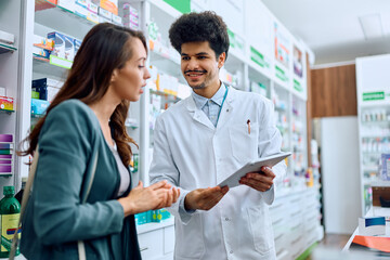Obraz premium Happy pharmacist and his female customer using touchpad in pharmacy.