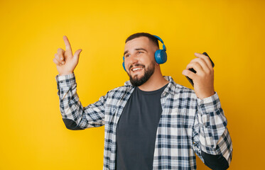 Naklejka premium Photo of a handsome guy listening to youth music in his ears, dancing a young man in a plaid shirt and trousers on a yellow background
