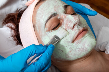 The cosmetologist applies a collagen booster on the client's face. Middle aged woman receiving spa...