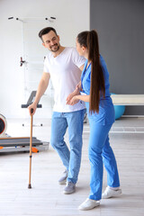 Female physiotherapist helping young man with walking stick in rehabilitation center