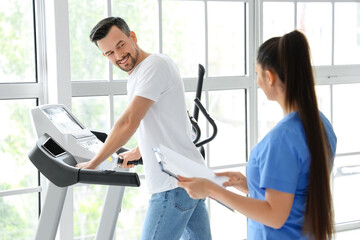 Obraz premium Female physiotherapist working with young man on treadmill in rehabilitation center