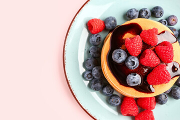 Plate with sweet pancakes and berries on pink background