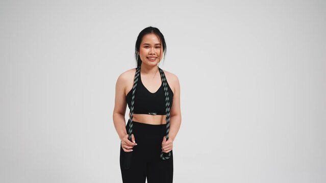Handsome asian woman holding skipping rope in black tracksuit against gray background in studio 