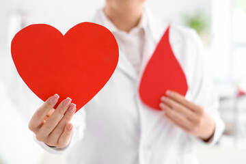 Female doctor with paper heart and blood drop in clinic, closeup