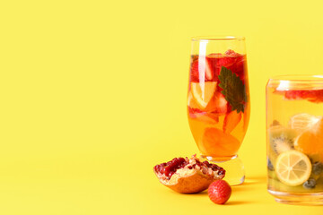 Glasses of infused water with different sliced fruits on yellow background