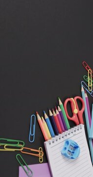 Vertical video of close up of school stationery with copy space on black background, in slow motion