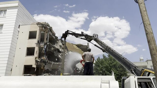 A demolition machine and a tanker that sprays water to prevent dust formation. The man spraying water.