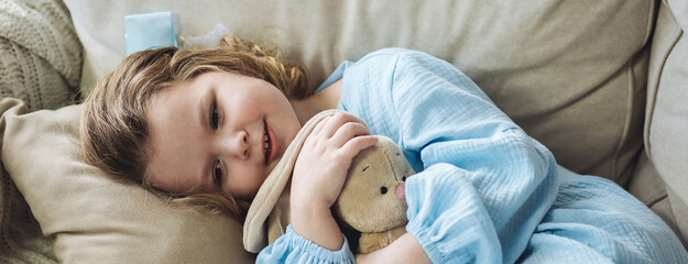 Cute little girl in blue dress on the sofa at home with her favourite toy, teddy rabbit. Concept of...